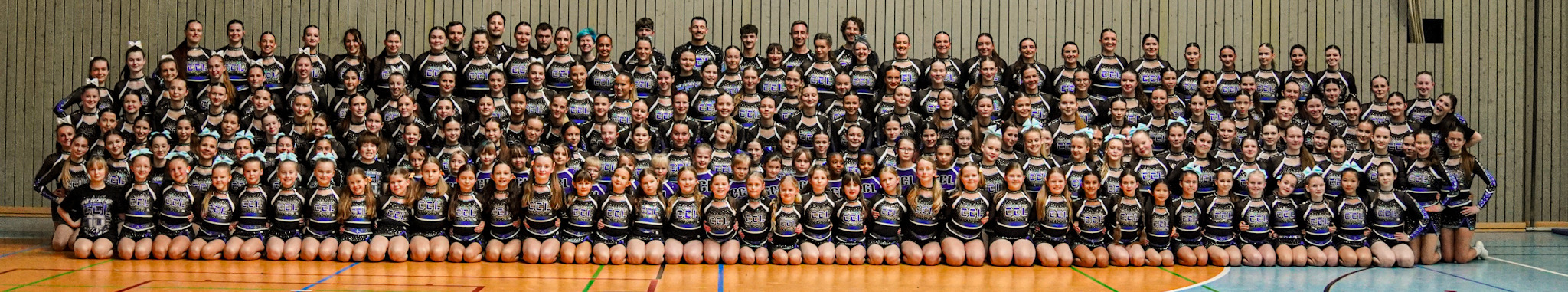 Gruppenfoto des Cheerleader Club Leipzig: alle Teams in Vereinsuniform in der Sporthalle